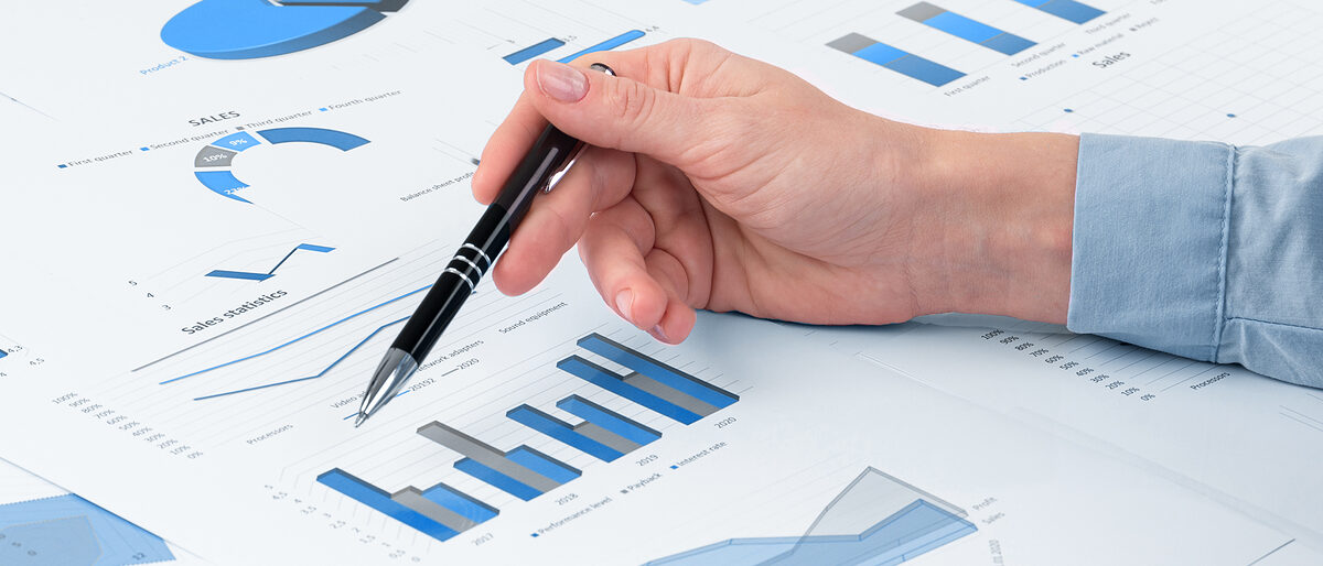 eine Hand mit Stift auf einem Blatt Papier mit statistischen Auswertungen