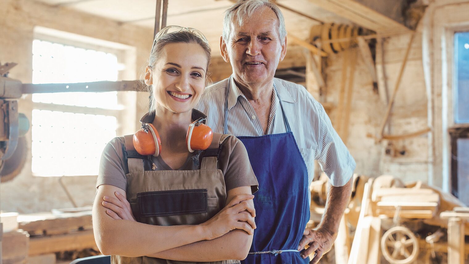 Senior master carpenter with his granddaughter in the wood workshop looking at camera